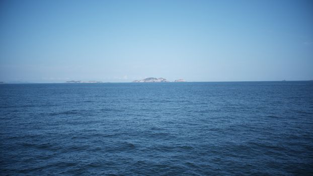 Calm ocean waters meet the horizon with distant islands under a clear blue sky.