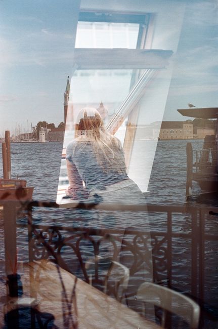 A woman looking through a window, capturing Venice's serene water reflections.