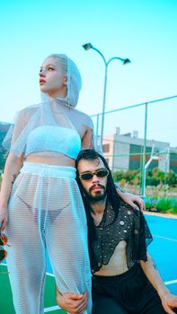 Stylish couple in mesh outfits posing outdoors on a tennis court, modern urban fashion.