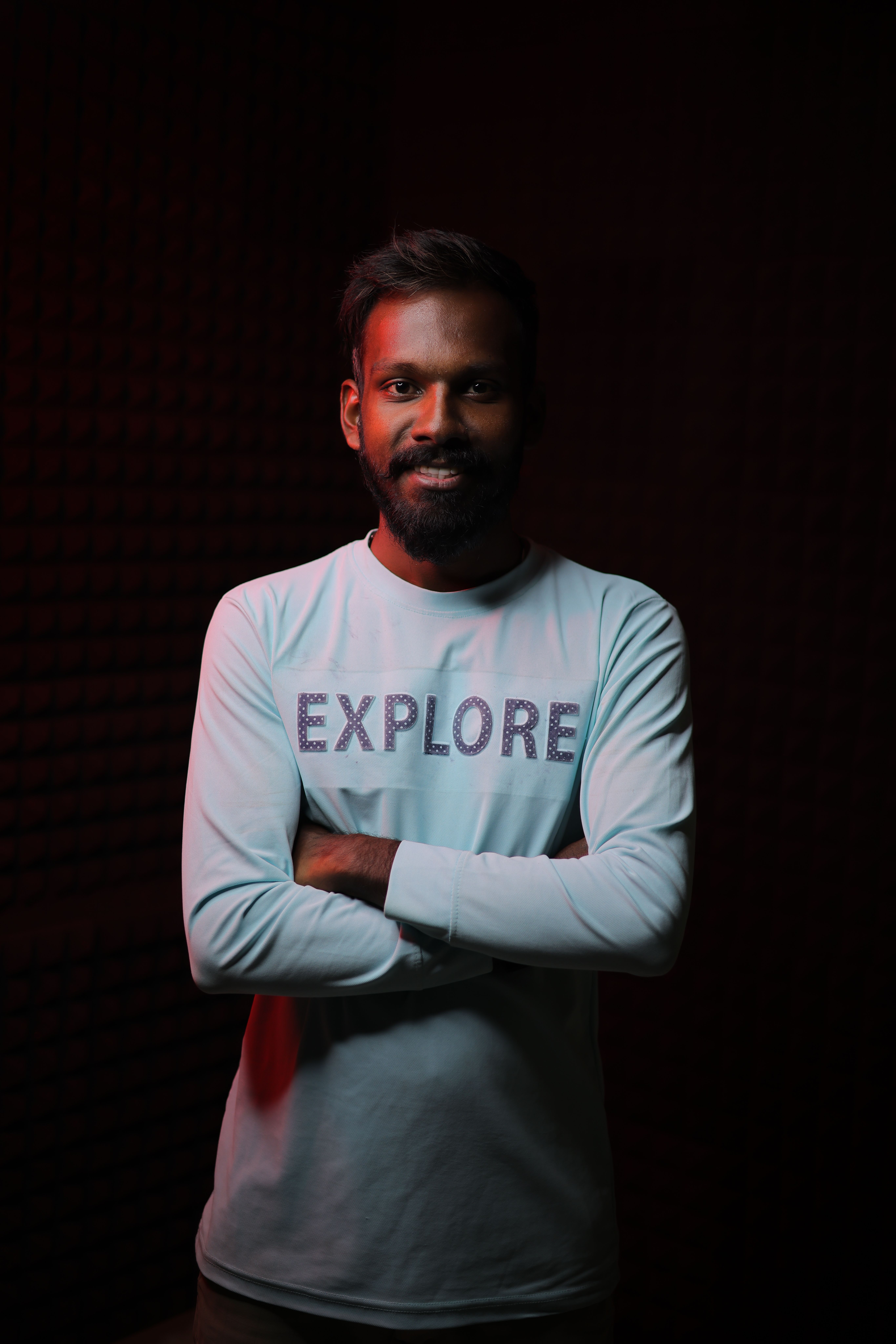 Portrait of a man in Rome with arms crossed wearing a shirt with 'Explore' text, set against a dark background.