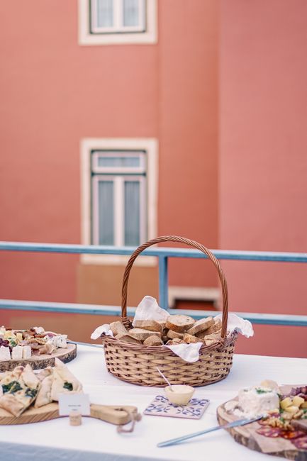 A basket of fresh bread on a table outdoors in Lisbon, with a pink building in the background.