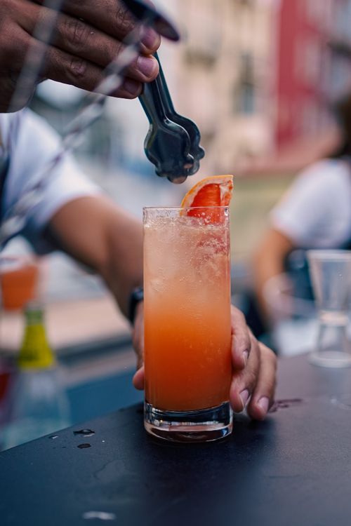 Free A bartender serving a fresh orange cocktail in a lively Lisbon outdoor setting. Stock Photo