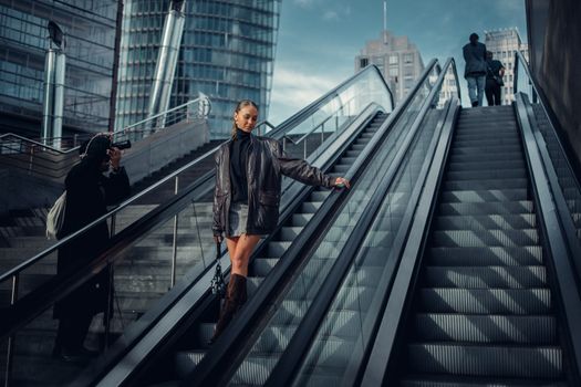 Stylish woman posing on urban escalator in a leather jacket for a modern fashion shoot.