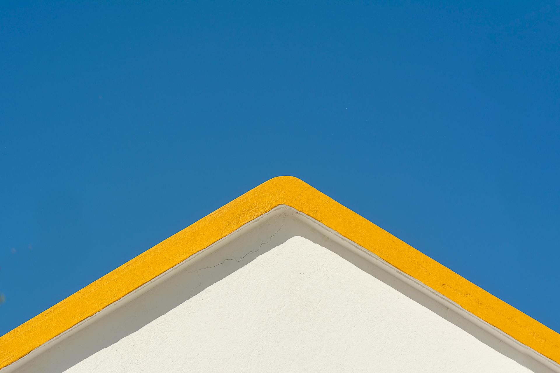 A minimalist house roof with yellow trim against a clear blue sky captures geometric simplicity.