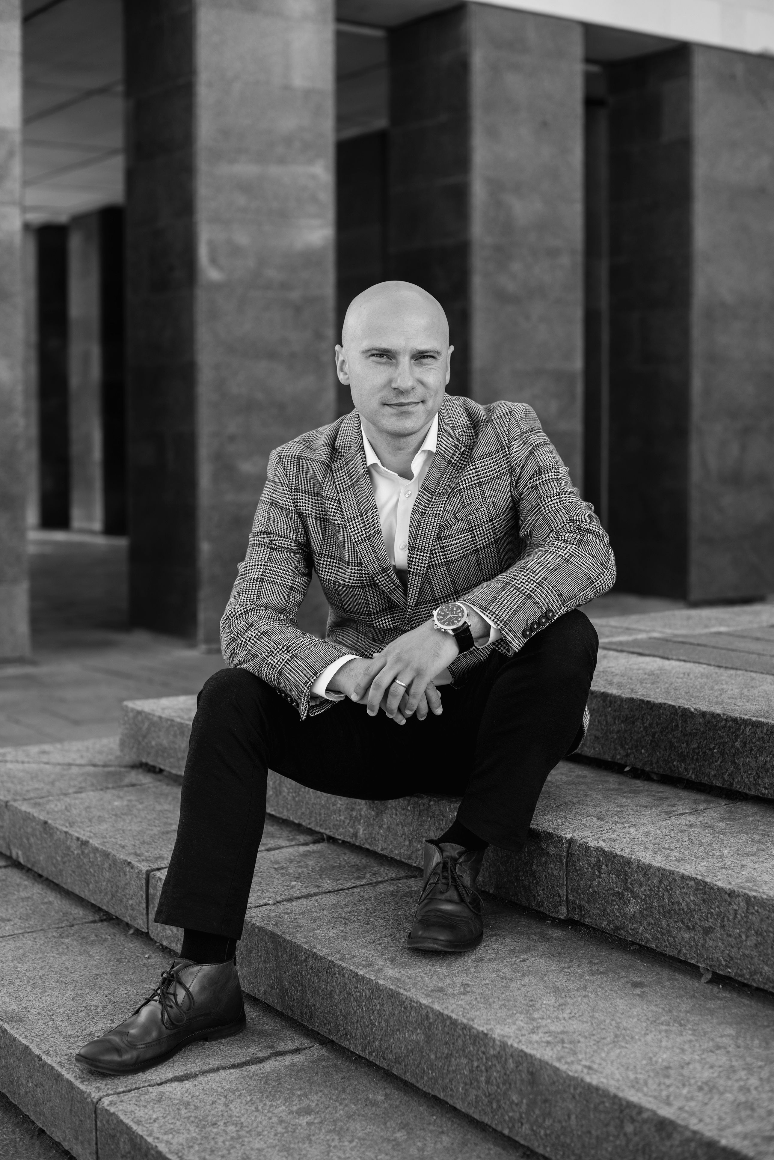 Black and white portrait of an elegant man sitting on steps in Kaunas, Lithuania.
