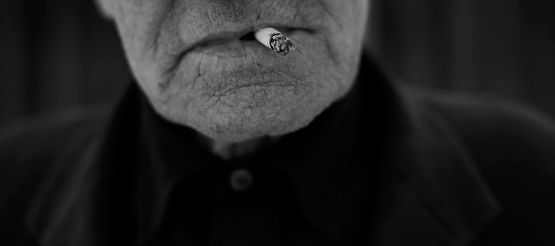 Black and white portrait of an elderly man smoking, highlighting facial details and texture.