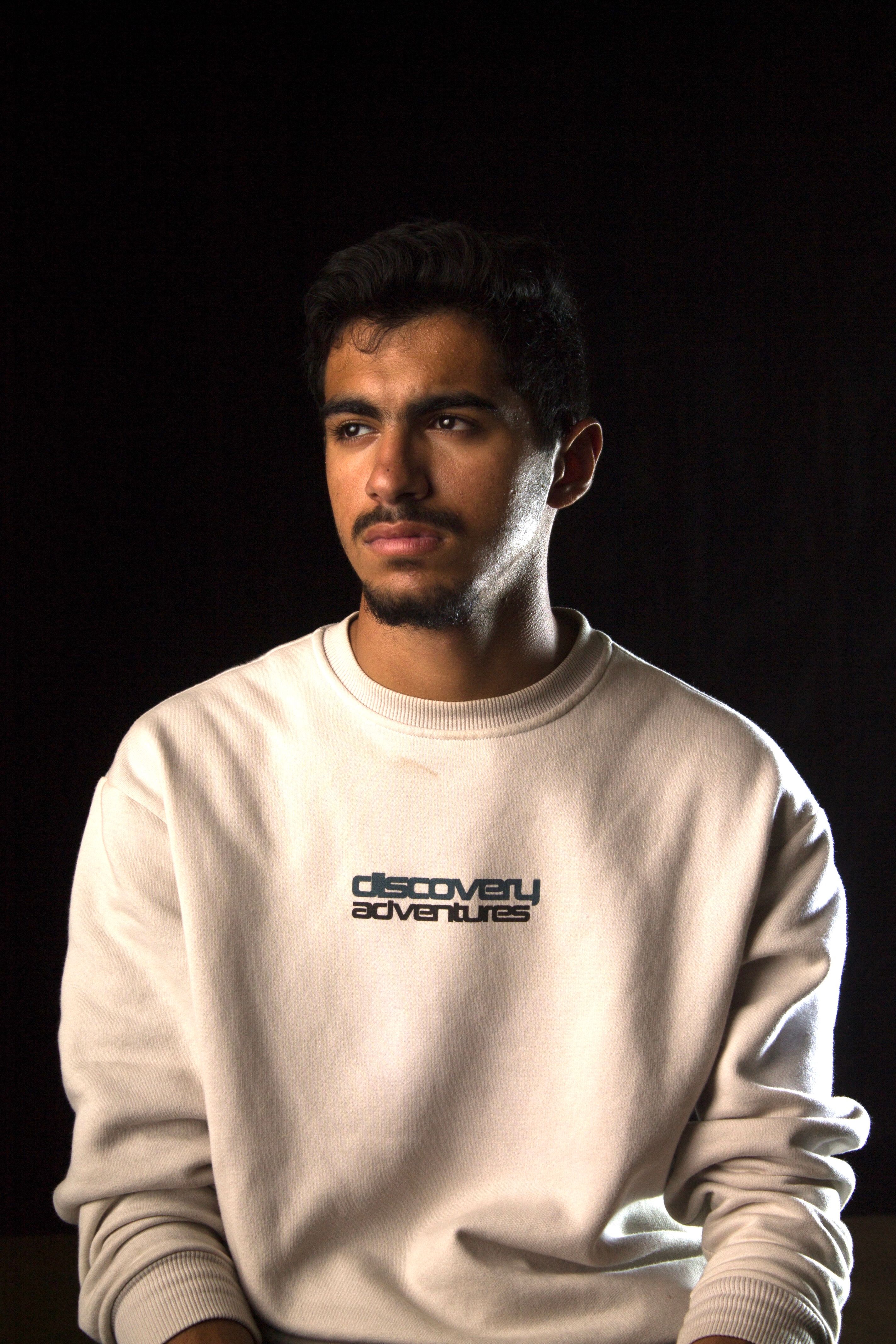 Studio portrait of a man wearing a casual sweatshirt with a dark background.