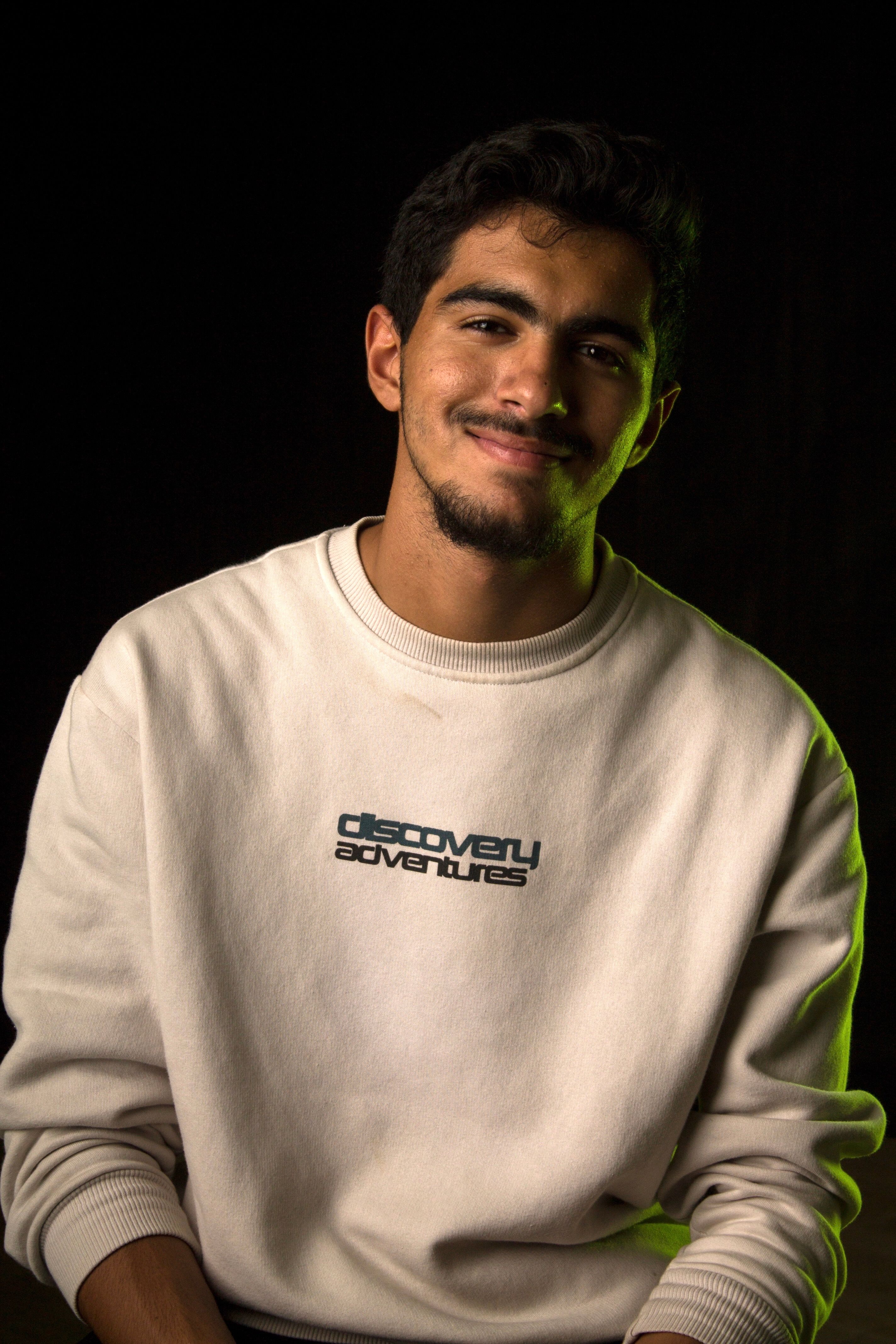 Portrait of a man smiling in a white sweatshirt with discovery adventures text against a dark background.