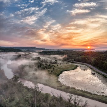 Stunning aerial view of a foggy sunrise over the serene landscape of Tell, Wisconsin, featuring a winding river and vibrant sunrise.