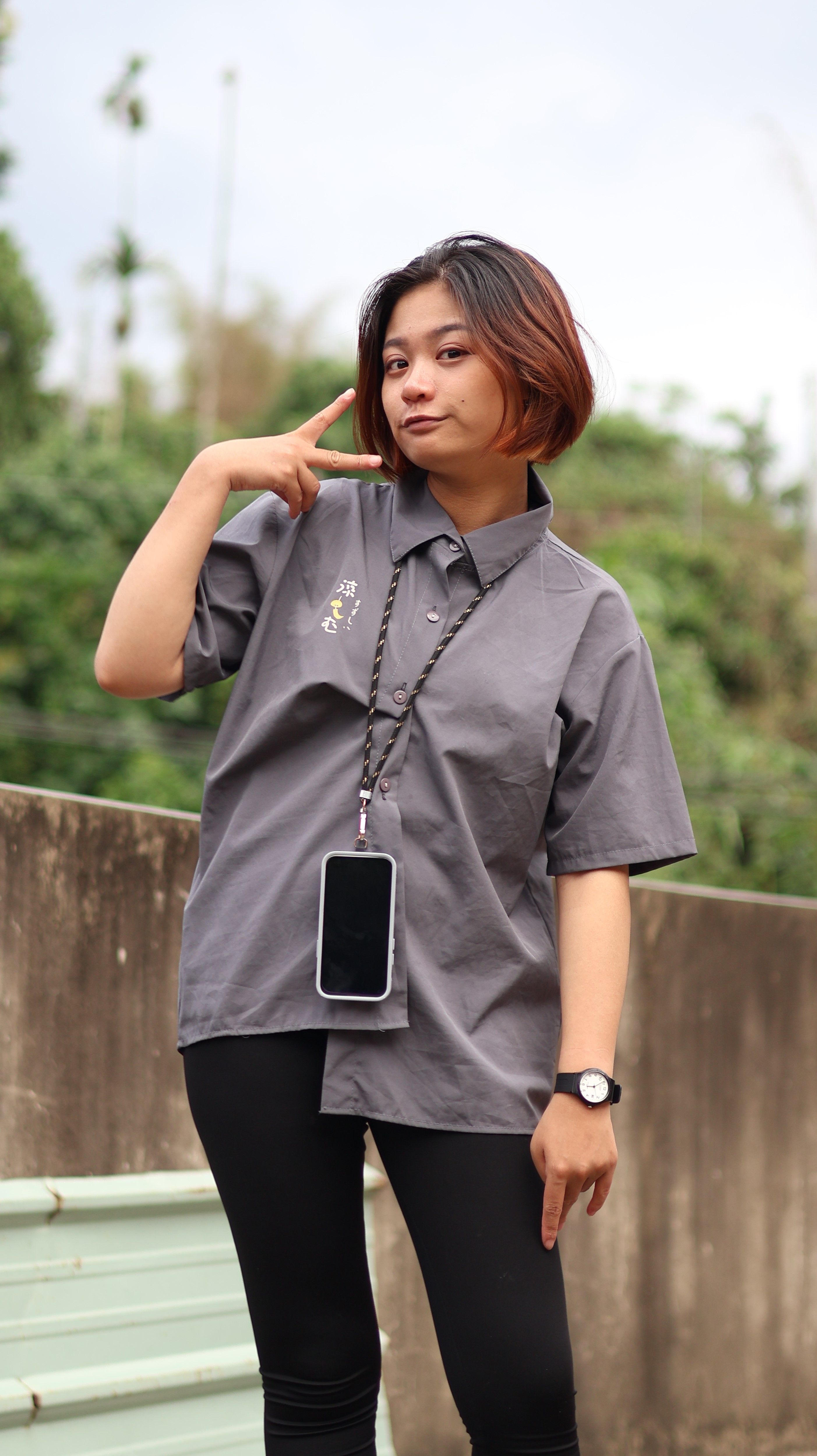 Young woman making a peace sign while standing outdoors in casual attire.