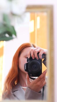 Young woman with long hair photographing herself in mirror reflection.