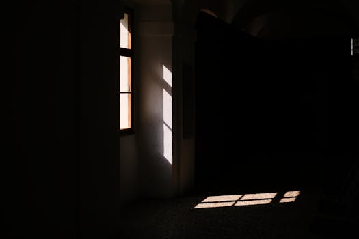 A dark room with sunlight streaming through a window, creating dramatic shadows.