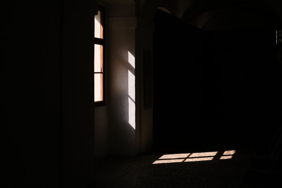 A dark room with sunlight streaming through a window, creating dramatic shadows.