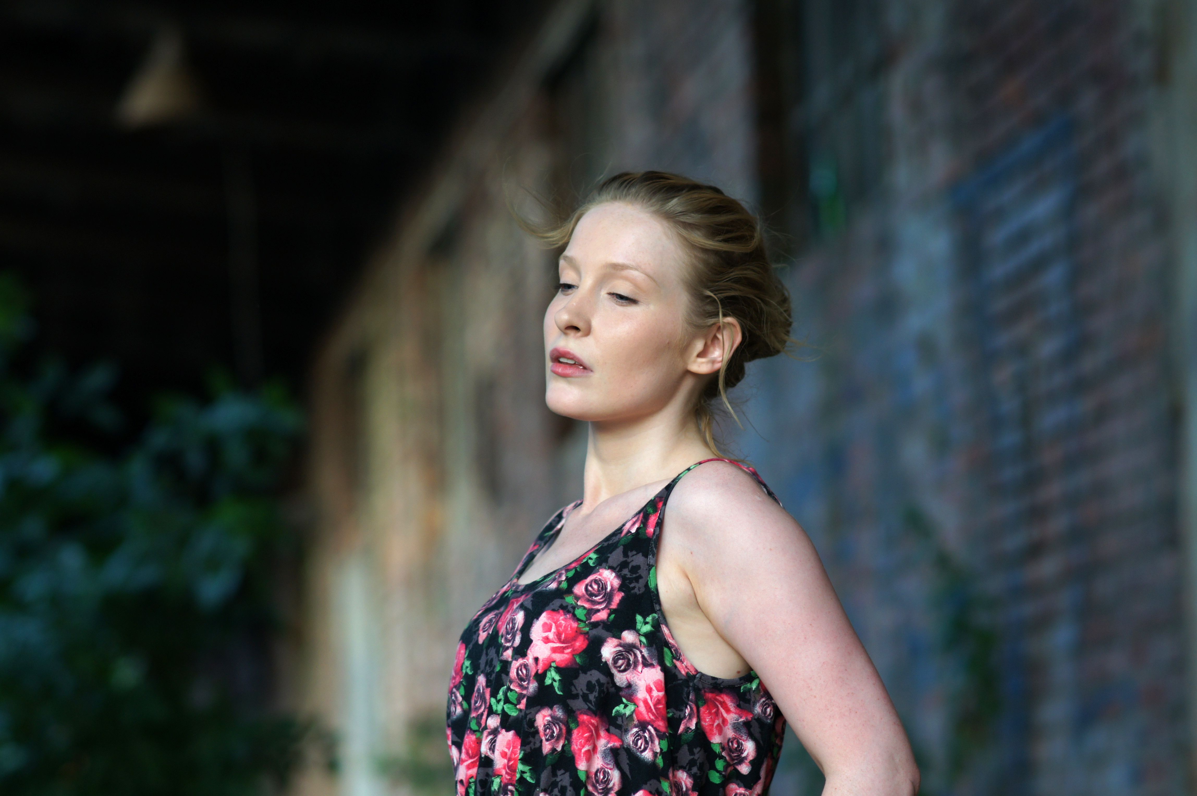 A woman in a floral dress is standing in front of an old brick building ...