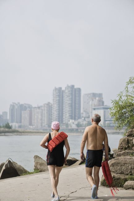 A senior couple enjoys a riverside walk with city skyscrapers in the background.