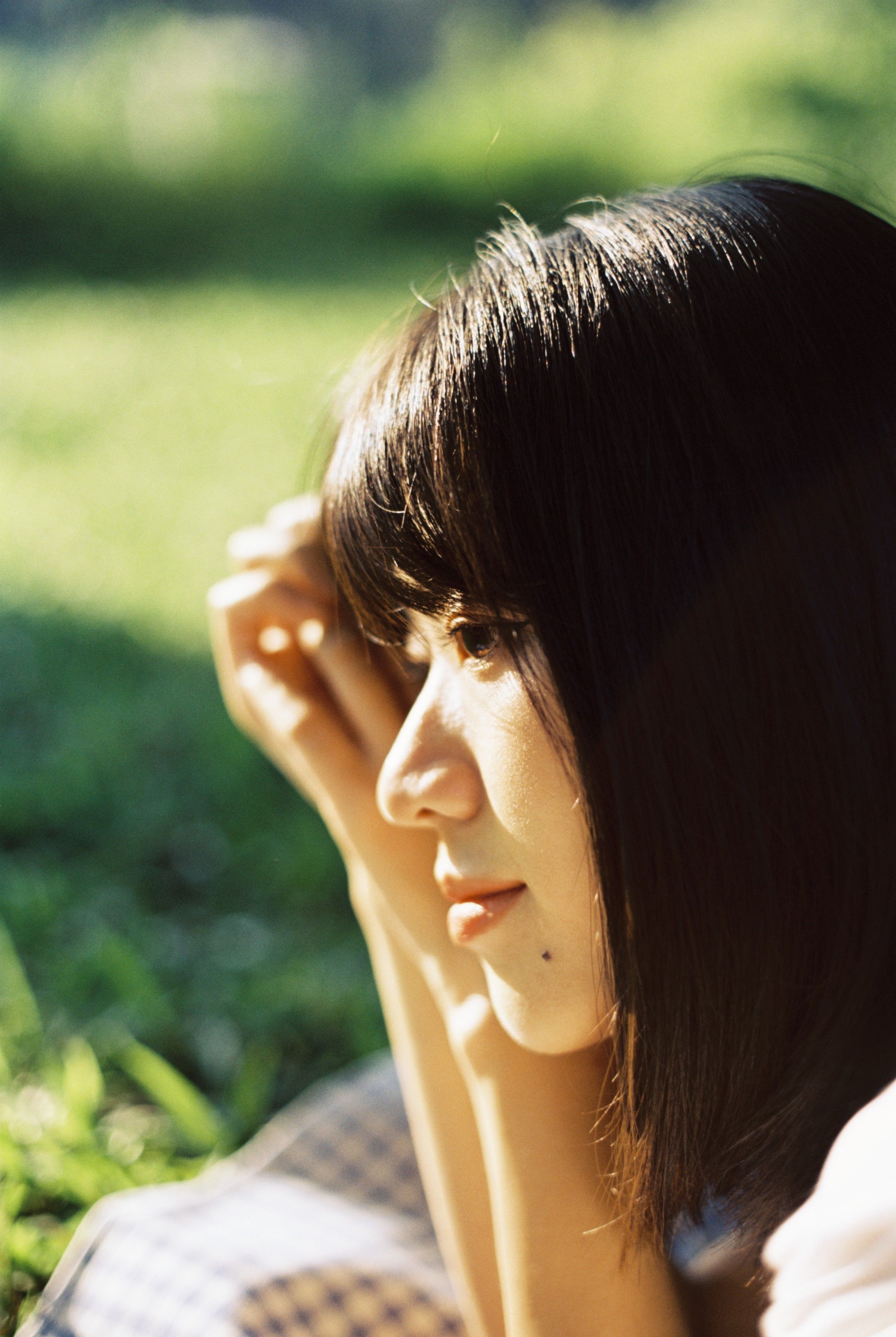 Close-up of a contemplative Asian woman with black hair, lying in a sunlit garden.