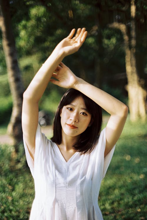 Young Woman Standing in a Park with Arms Raised 