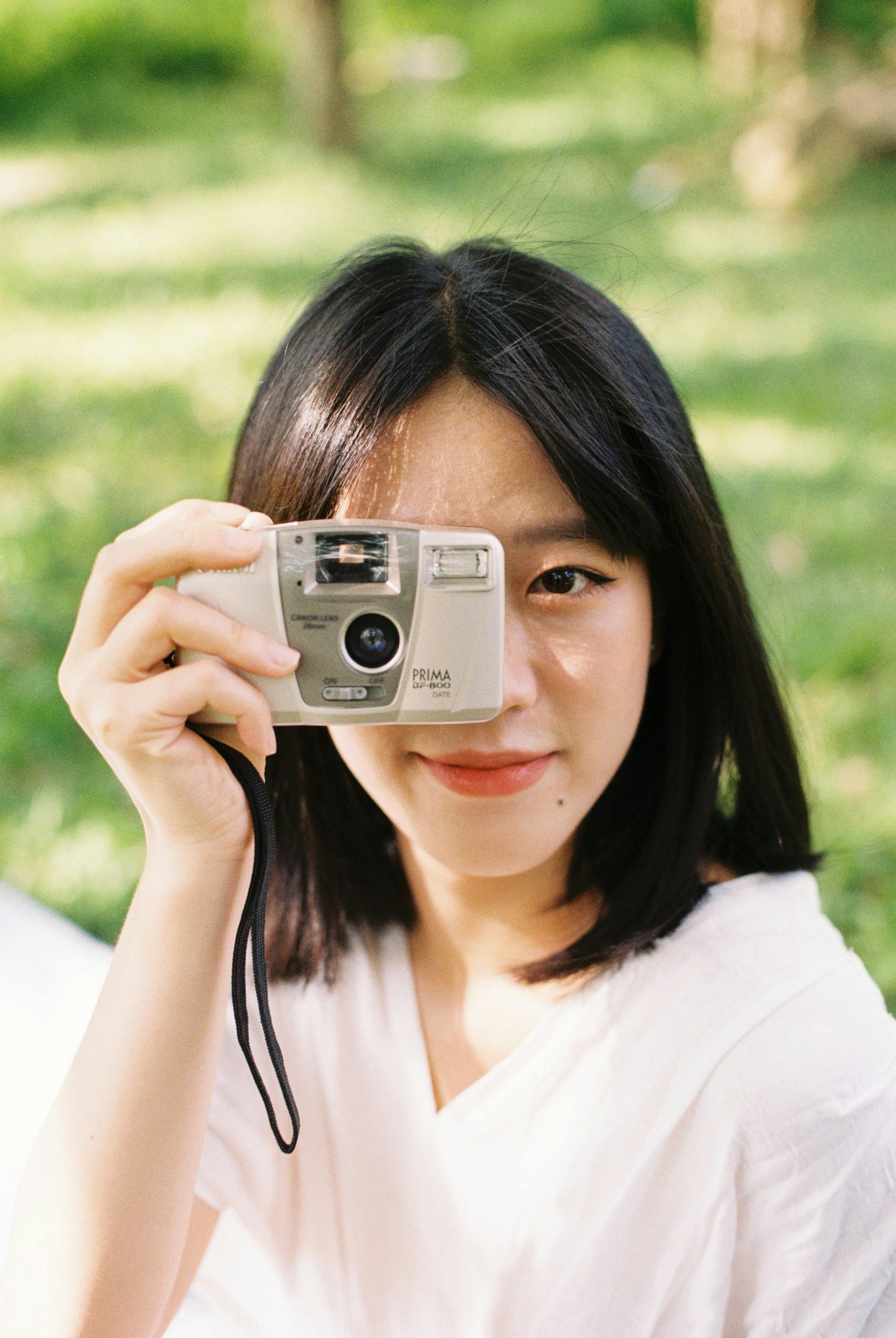 Smiling Young Woman Looking Through an Amateur Camera · Free Stock Photo