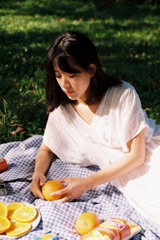 A young woman in a white sundress at a sunny picnic with oranges.