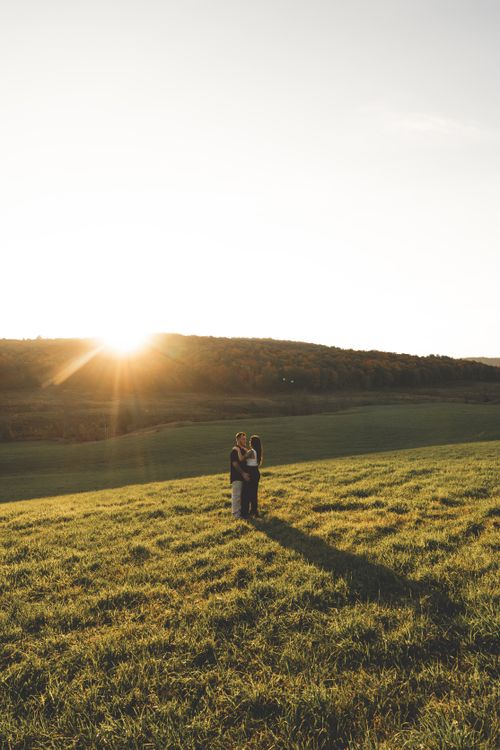 Free A couple stands embracing in a vast rural meadow during a beautiful sunset. Stock Photo
