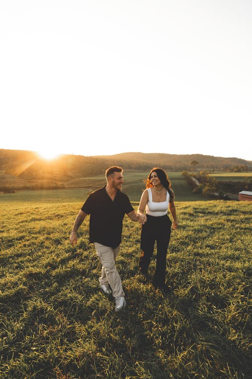 Smiling Couple Walking on Grassland at Sunset