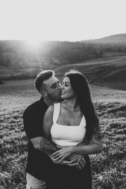 Black and white photo of a couple embracing in a meadow at sunset, expressing love and romance.