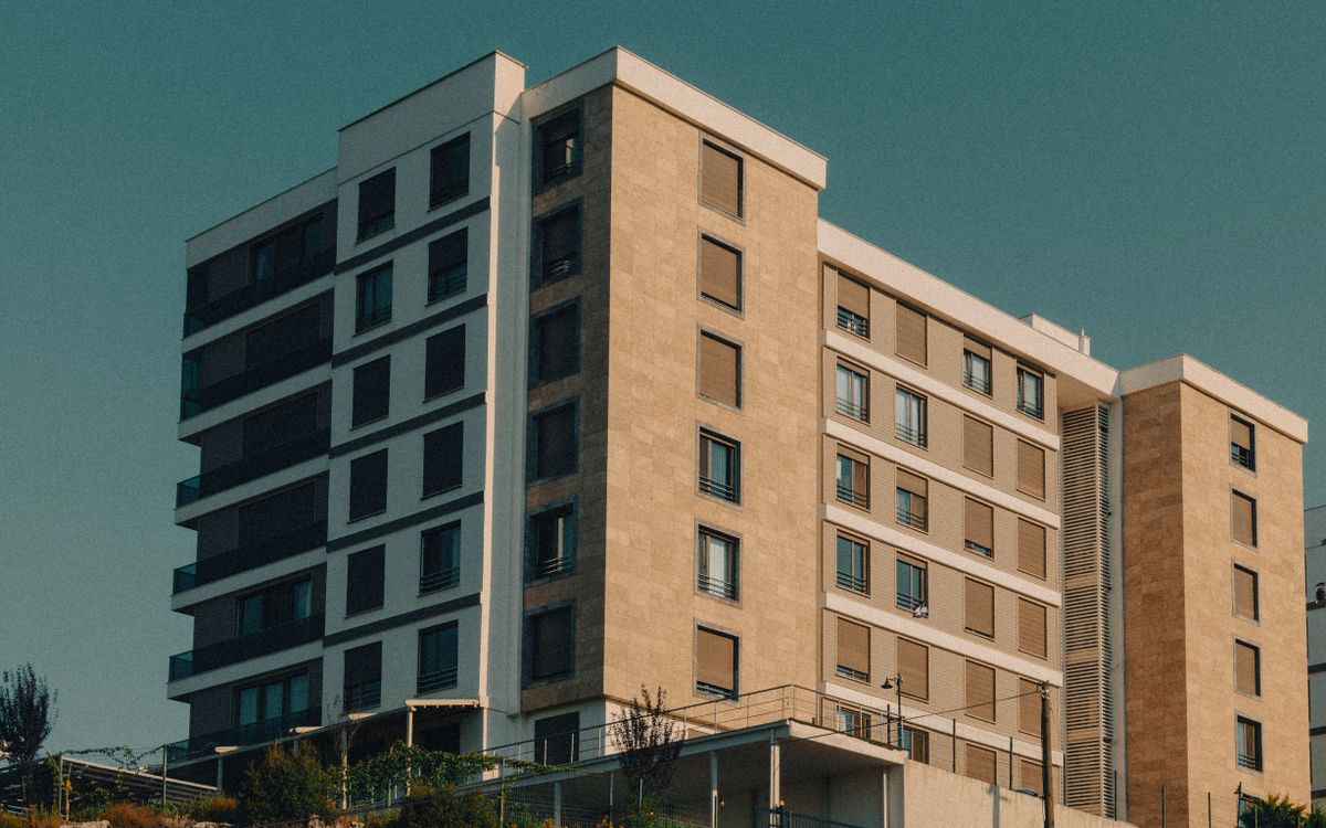 Modern apartment building with a warm beige facade rising against a clear sky, calm negative space on the left for the headline