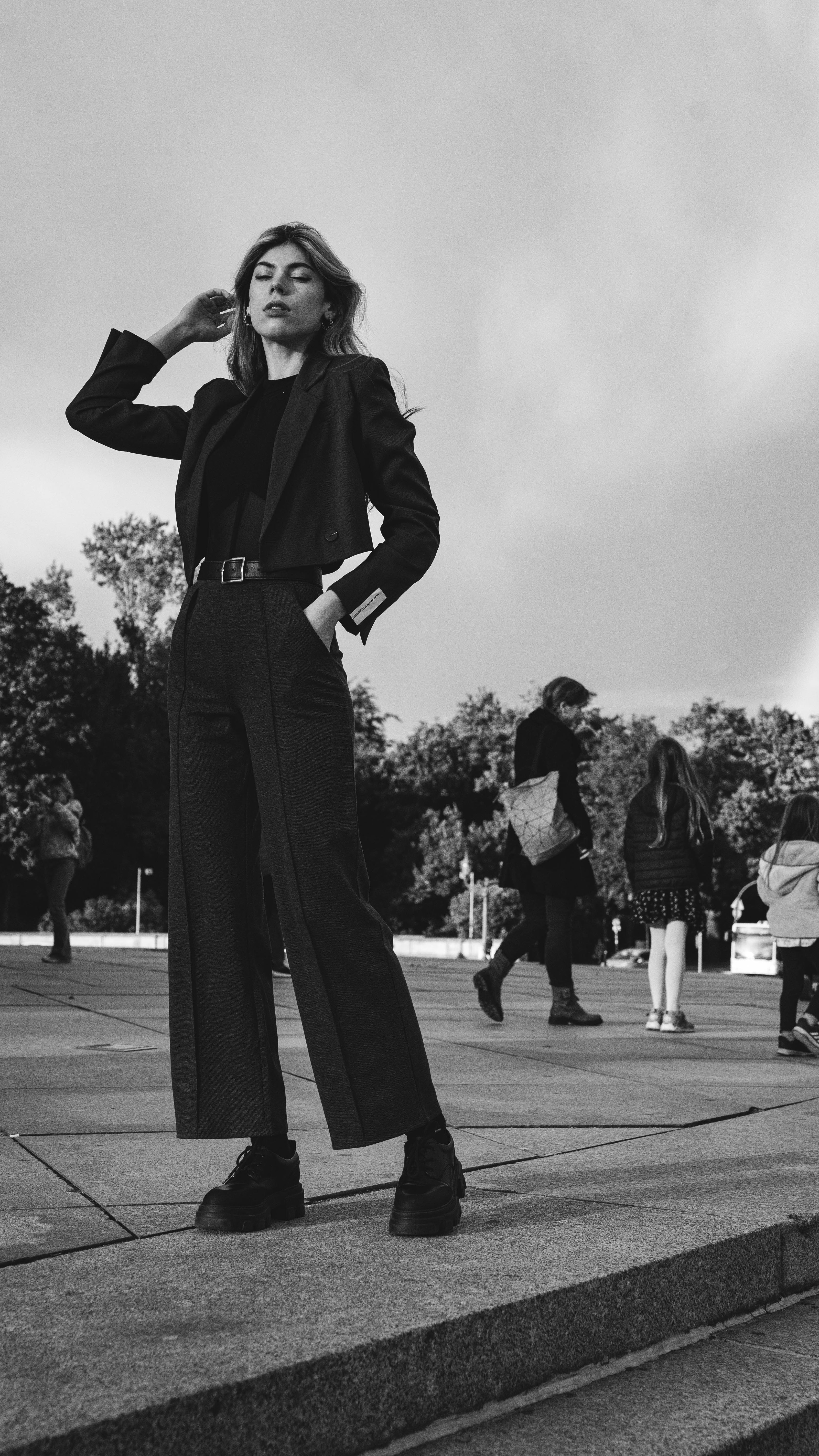 Mulher elegante posando com um blazer estiloso ao ar livre, exibindo moda moderna em preto e branco.