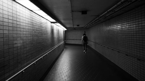 Free A lone man walks through a monochrome subway tunnel, evoking urban solitude. Stock Photo