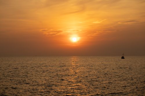 Free A tranquil scene of a boat on a calm sea during a beautiful orange sunset. Stock Photo