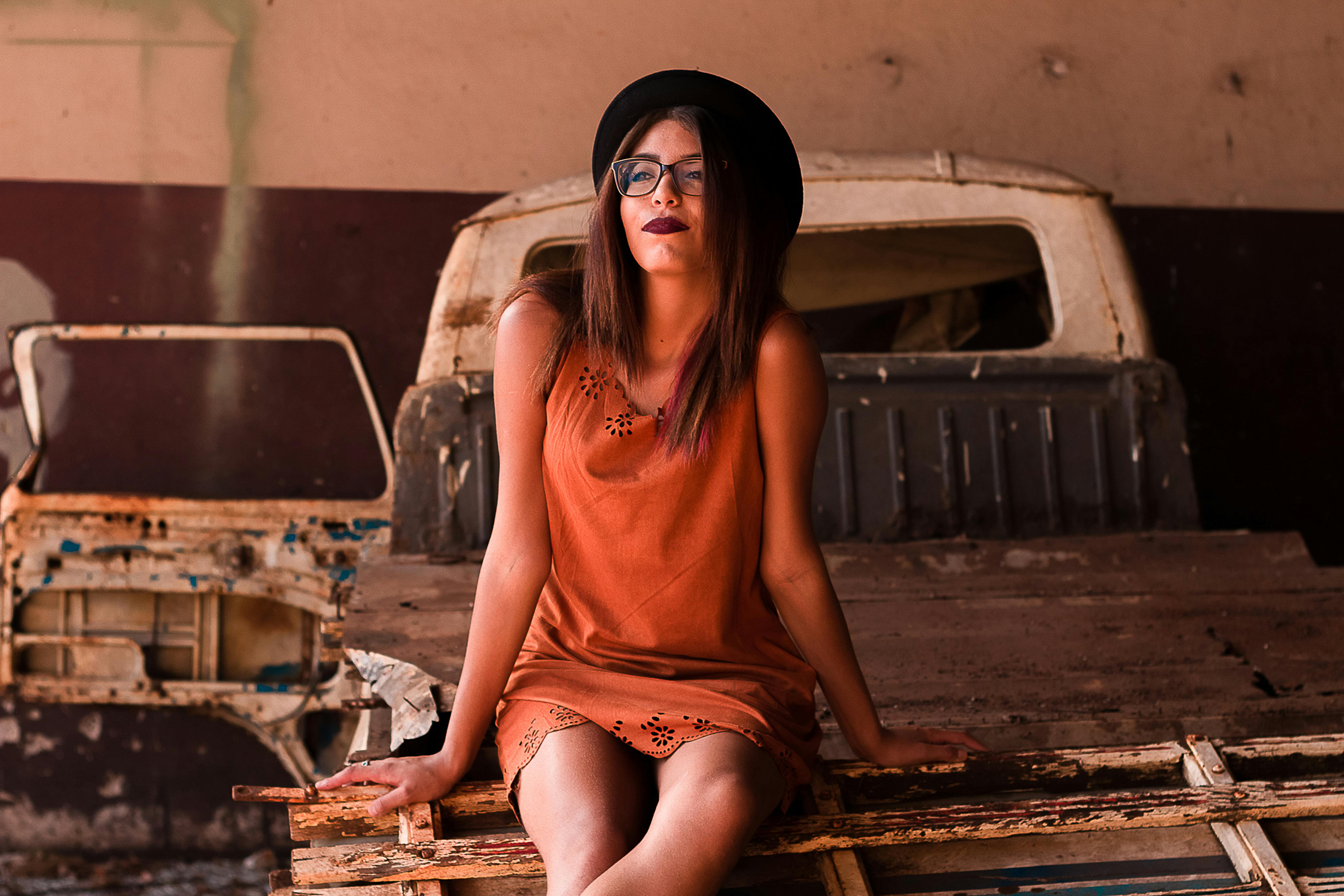 在城市环境中，一位戴眼镜和帽子的时尚女子正站在一辆生锈的卡车上摆姿势