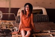 在城市环境中，一位戴眼镜和帽子的时尚女子正站在一辆生锈的卡车上摆姿势