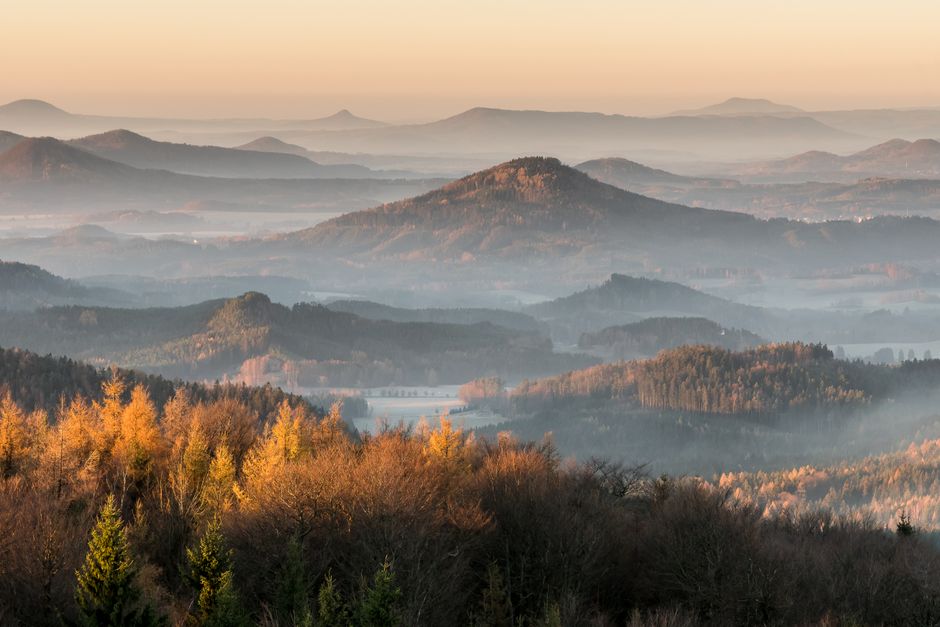 Vast mountain range shrouded in fog during sunrise in autumn, offering a serene and scenic vista.