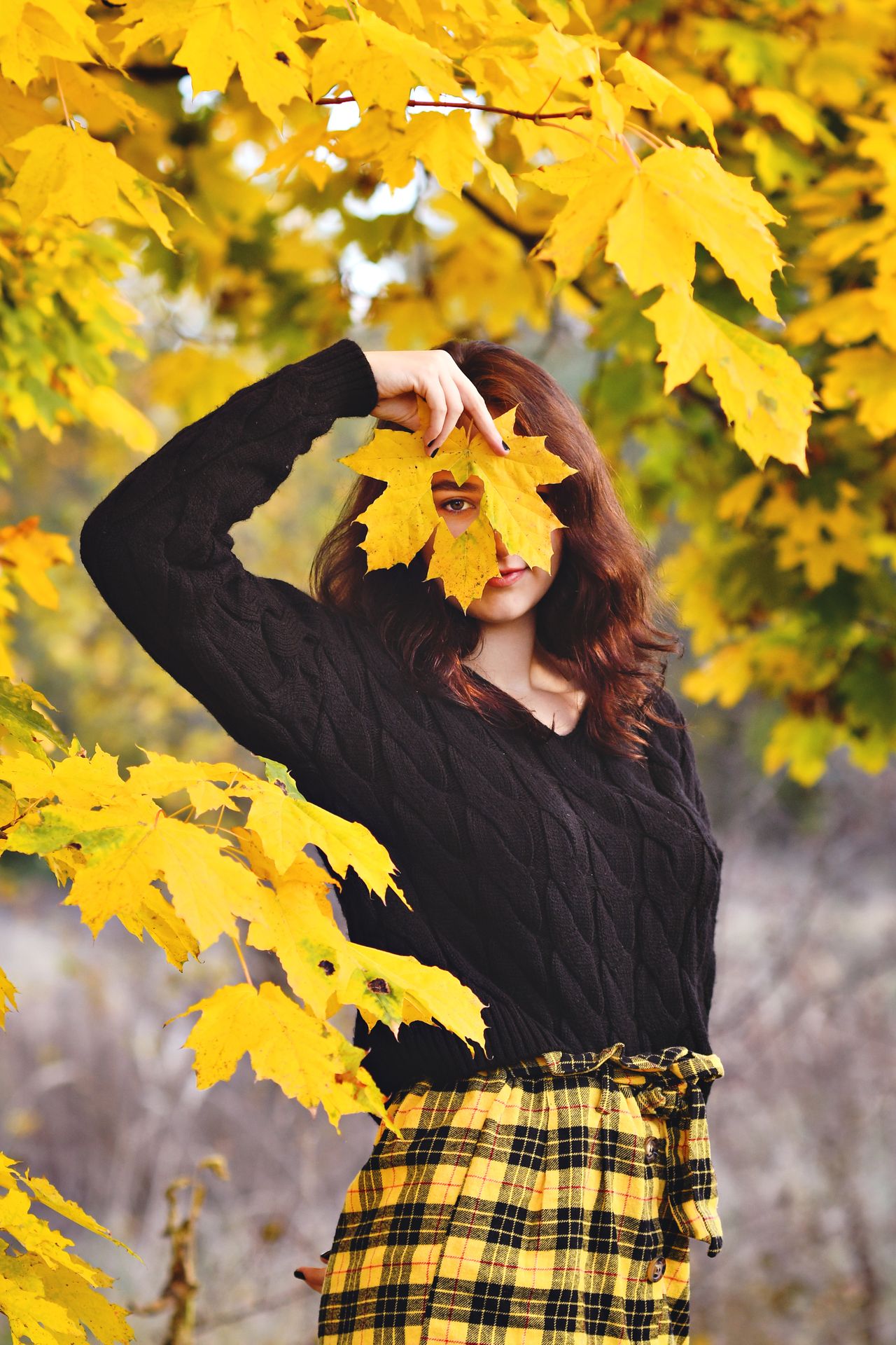 Woman in a black cable-knit sweater and yellow plaid skirt among autumn leaves