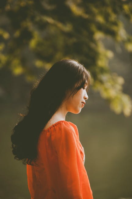 Side profile of an Asian woman in nature, wearing a red dress. Warm and serene.