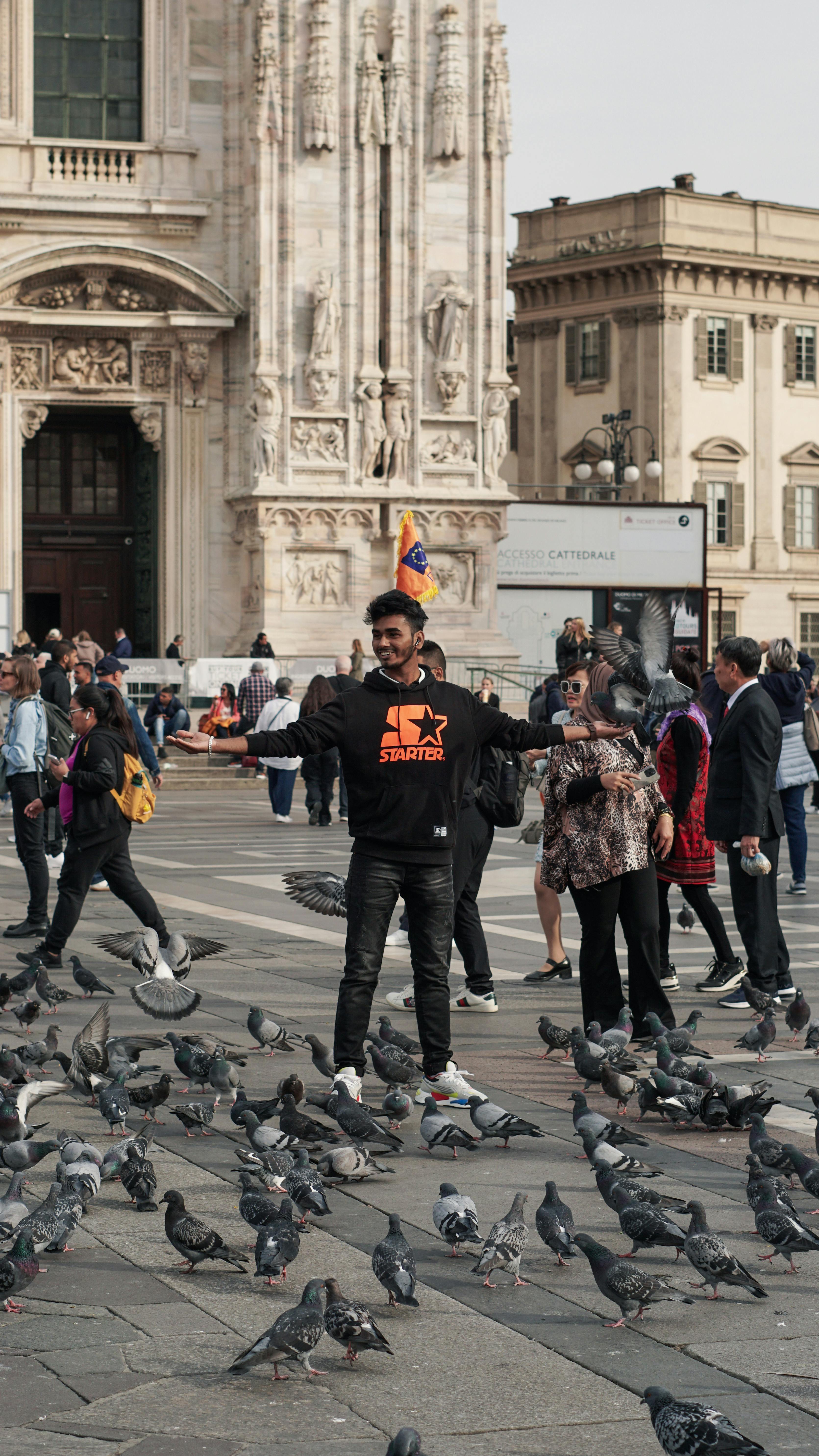 Tourist surrounded by pigeons at the iconic Piazza del Duomo in Milan, Italy.