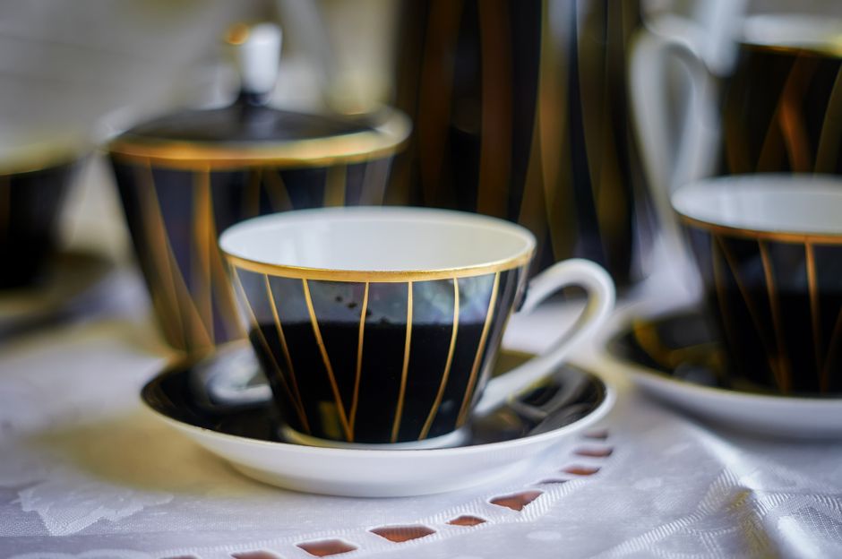 Sophisticated porcelain tea cup set against white cloth, featuring black and gold design.
