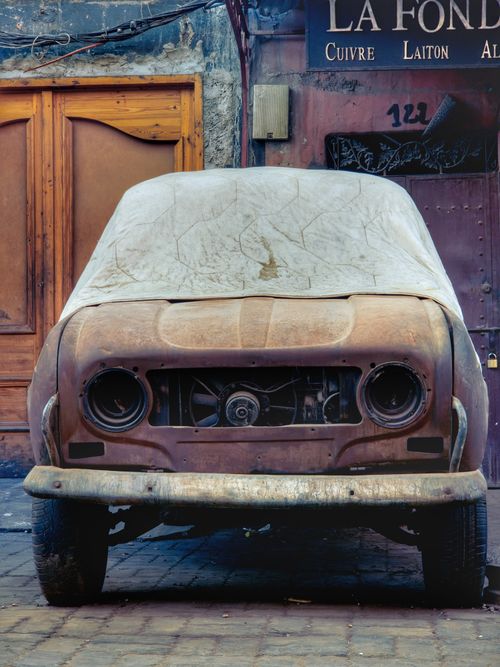 Free Front view of an old rusty car covered by a cloth in a Moroccan city street. Stock Photo