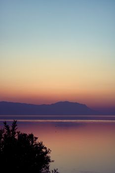 A breathtaking sunset over a tranquil lake with distant mountains, capturing a calm and peaceful atmosphere.