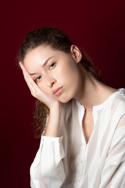 A thoughtful woman posing with hand on face against a deep red background.