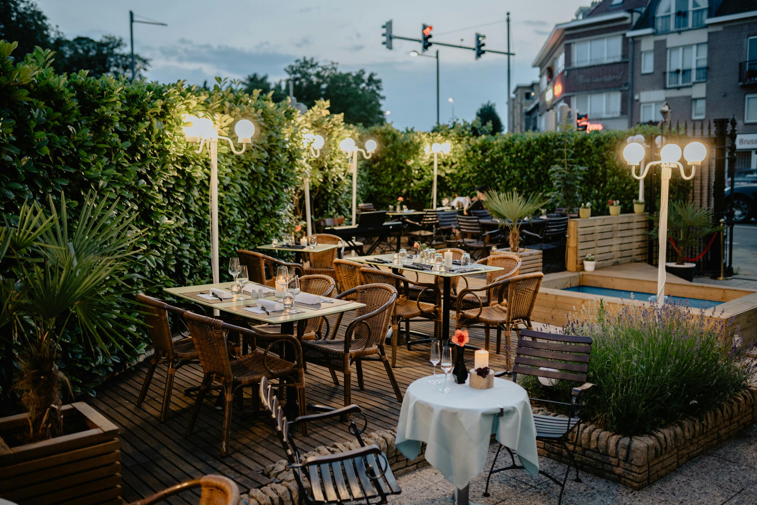 A cozy outdoor restaurant terrace setup with wooden furniture and warm lighting in a serene urban setting.