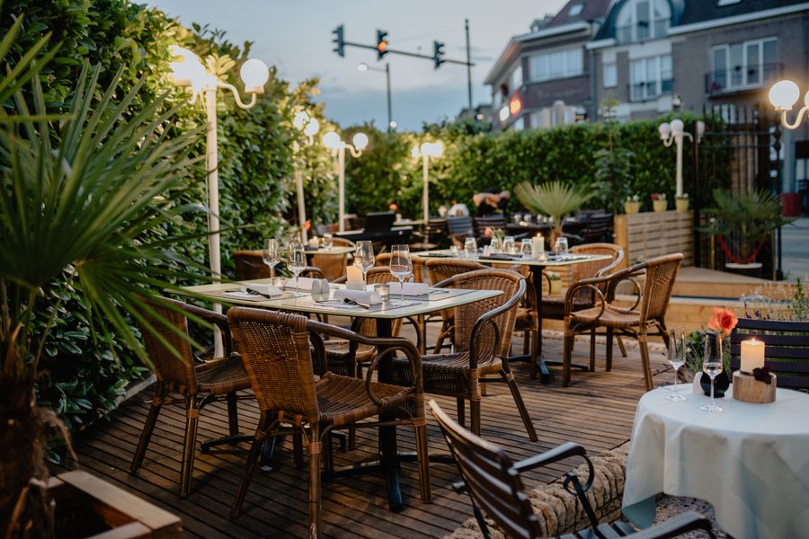 An open-air restaurant terrace with rattan chairs, white tablecloths and tropical planting