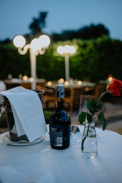 Free Cozy outdoor dining scene with wine, a single rose, and soft evening lighting. Stock Photo