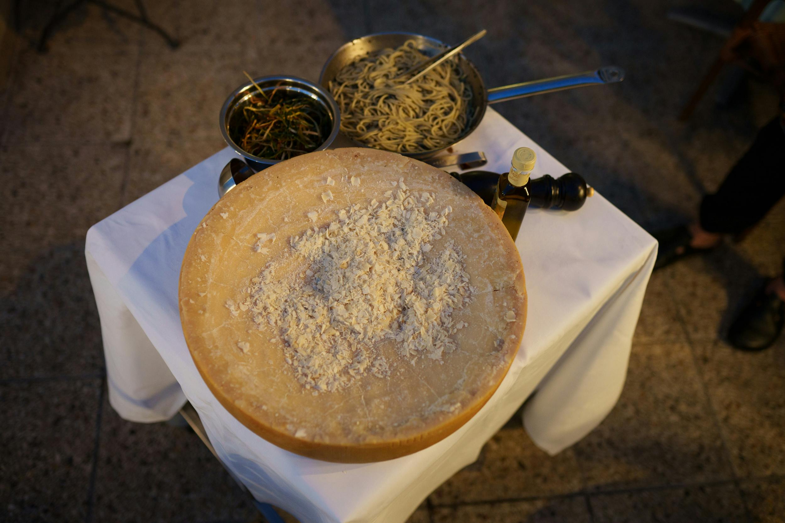 Pecorino Romano Cheese On A Wooden Cutting Board With A Grater And Pasta In The Background
