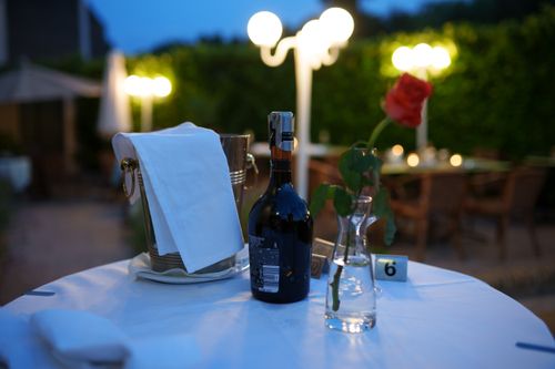 Free Charming evening setting on a patio with wine bottle, rose, and ambient lights for an elegant dining experience. Stock Photo