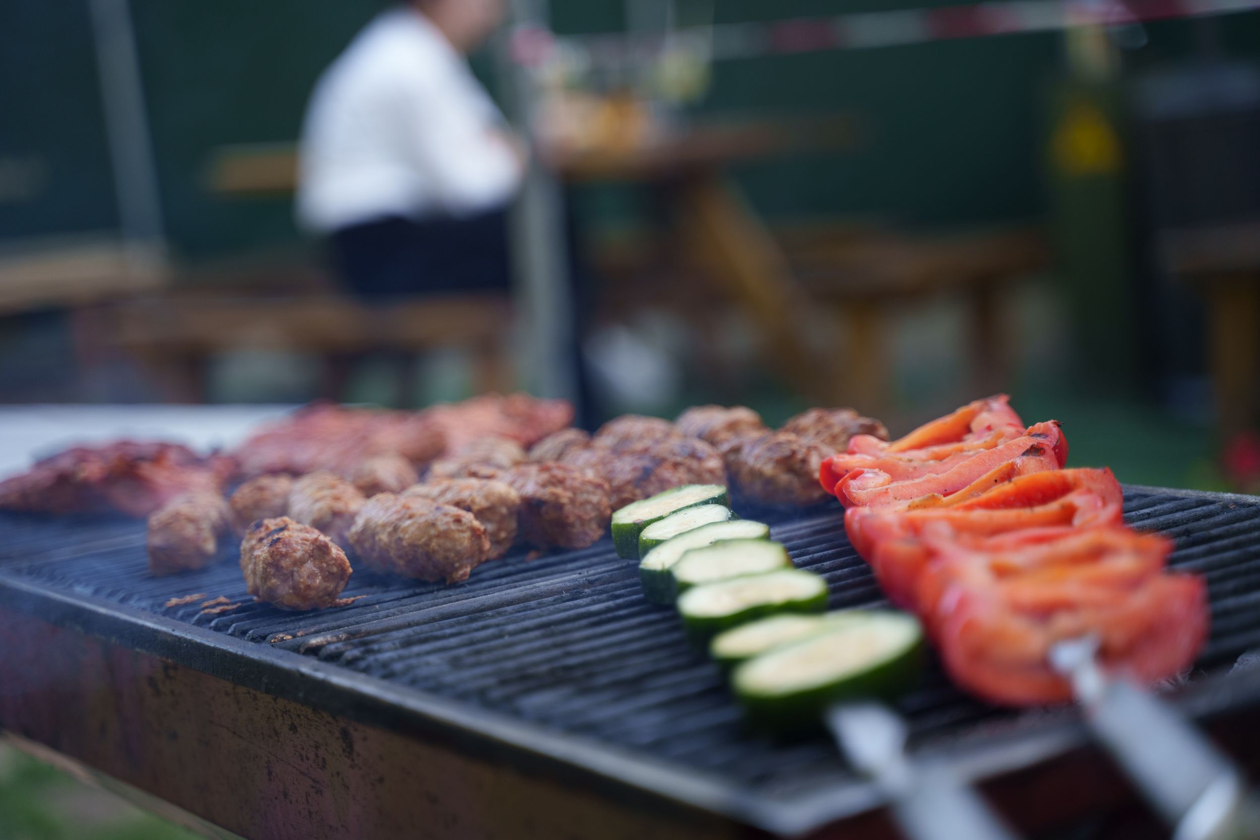 Close-up of a barbecue grill with meats and vegetables sizzling outdoors.