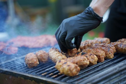 Close-up of a hand wearing a glove, grilling meat on an outdoor barbecue grill.