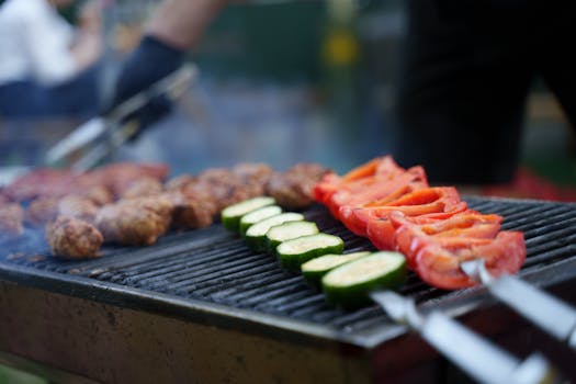Close-up of a BBQ grill with grilled meat and colorful vegetables outdoors.