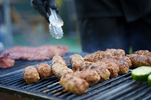 Grilled sausages and meat on a barbecue with tongs and vegetables.