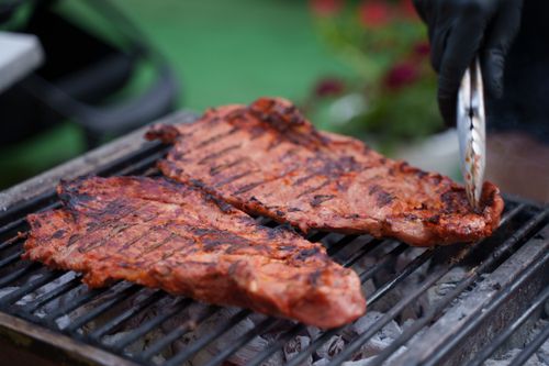 Free Close-up of sizzling ribs on an outdoor barbecue grill, with tongs grabbing meat. Stock Photo